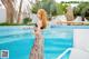 A woman in a long dress standing next to a swimming pool.