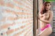 A woman in a pink lingerie leaning against a brick wall.