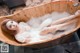 A woman laying in a wooden bathtub filled with foam.